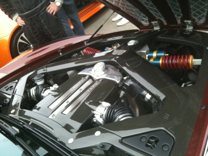 Pistonheads - The image captures a close-up view of the engine compartment of a sports car, showcasing the meticulous arrangement of components. The hood is open, revealing a complex array of pipes, wires, and mechanical parts. The car's interior, equipped with three pedals, indicates it's a manual-shift vehicle. The overall scene suggests a passion for automotive design and engineering. The focus on the engine hints at a precision that is both admirable and extreme.