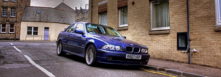 Large Pistonheads Smoker Barges - The image shows a blue BMW car parked on the street in front of a building. The building appears to be a residential or possibly a small business building as there are curtains visible through the windows. The street appears to be isolated, with no other vehicles in sight, emphasizing the BMW as the main focus of the image. The weather seems to be overcast, giving a somewhat dramatic feel to the scene. The lighting suggests it could be early morning or late afternoon, adding to the desolate atmosphere of the street.