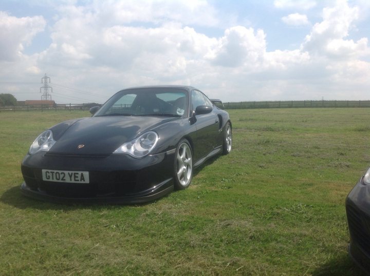 GT2 - Page 53 - Porsche General - PistonHeads - The image features a black Porsche sports car parked in a pasture, which is likely a field of grass, with power lines visible in the background. The car is positioned facing the left side of the image and is captured under an overcast sky with some clouds. The license plate of the car displays "GT02 YEA," indicating that it is a Euro-specification vehicle, possibly of a 2013 model year.