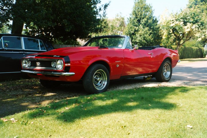 Musclepony Porn Pistonheads Poll - The image depicts a vibrant scene in a residential area. The most striking feature is a red Mustang muscle car, parked prominently on the grass. A person is visible in the distance, adding a touch of human element to the scene. In the background, shrubbery and trees line the street, providing a natural backdrop to the vehicles and residents.