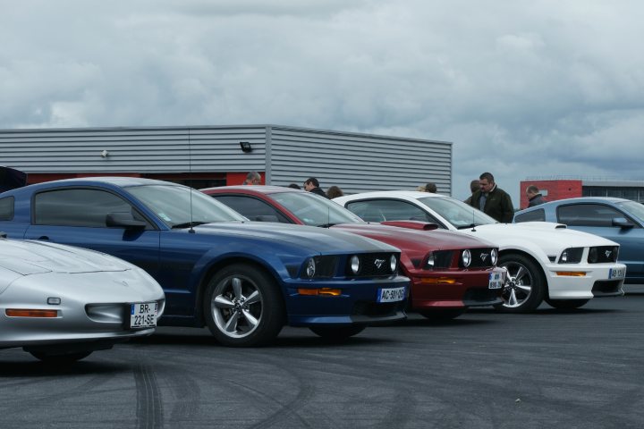 Things they dont tell you when you SELL an Elise - Page 1 - Elise/Exige/Europa/340R - PistonHeads - The image presents a display of classic muscle cars parked in a row at an indoor garage. The muscle cars are predominantly blue, with the odd white car among them. The exhaust fumes from the cars' engines, indicative of the shiny black top road that appears to be soaking wet, suggesting that it has recently rained. The cars show various models and vintages, adding to the overall classic look of the display. The photograph provides a detailed view of these vehicles, emphasizing their sleek designs and vibrant color schemes.