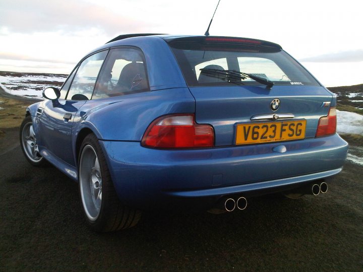 Itr Coupe Bmw Pistonheads Honda - The image features a blue BMW car from a rear, highway-oriented angle. The car appears to be a two-door version, with distinctive BMW emblems and design elements on the trunk door and taillights. The license plate reads "V623 FSFG," indicating some details such as registration and possibly the model or engine specifications. The car is set on a road with a patch of snow on its right side, suggesting a location or travel during a season with colder weather. The skies are overcast, and the lighting in the photograph provides a natural ambiance.