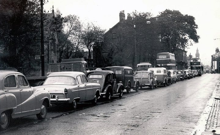 A 'period' classics pictures thread (Mk II) - Page 325 - Classic Cars and Yesterday's Heroes - PistonHeads UK - The image is a black and white photograph depicting a street scene with numerous vintage cars parked on the sides. It appears to be a busy street as evidenced by the presence of multiple cars, both stationary and in motion. There are also two buses visible, adding to the sense of urban congestion. The architecture and style of the vehicles suggest that this photo was taken in the mid-20th century. The sky is overcast, hinting at a possibly gloomy or rainy day. The overall composition of the image captures a moment of everyday life during a time when automobiles were a prominent feature of urban landscapes.