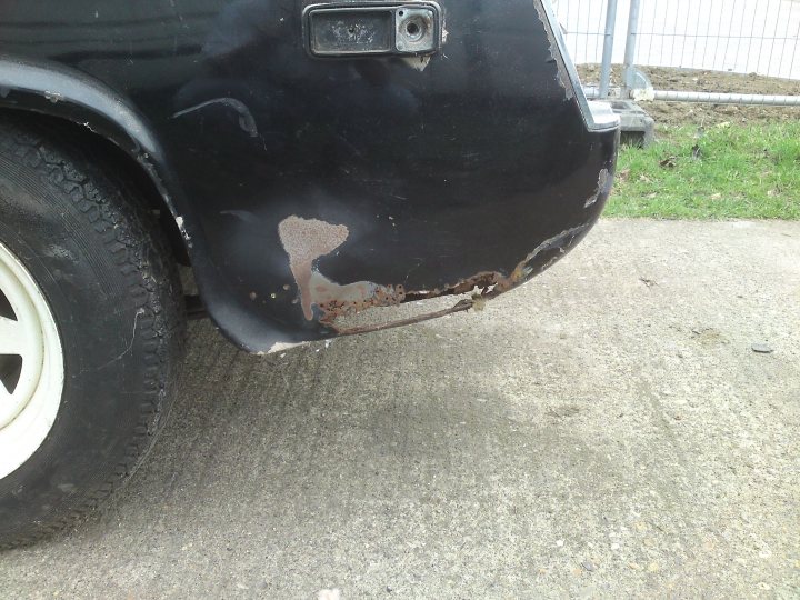 Sprite Austin Healey Pistonheads - This image shows the rear bumper of a black vehicle. The bumper appears to be old and worn, with signs of rust, particularly on the furthest point of the bumper from the camera angle. There are stains on the surface, suggesting exposure to elements over time. The tire in the foreground is in good condition, showing distinct treads and a sharp sidewall.