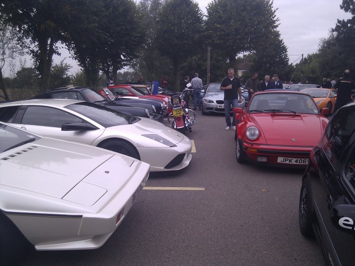 The Hare Roxwell meets ended? - Page 1 - Kent & Essex - PistonHeads - The image captures an outdoor scene where a gathering of luxury, sports, and convertible cars is taking place on a street. A total of eight cars are prominently displayed, with a variety of colors including red, white, black, and silver. Several people can be seen walking among the vehicles and observing the cars. The setting appears to be a car show or event, with the vehicles parked tightly together.