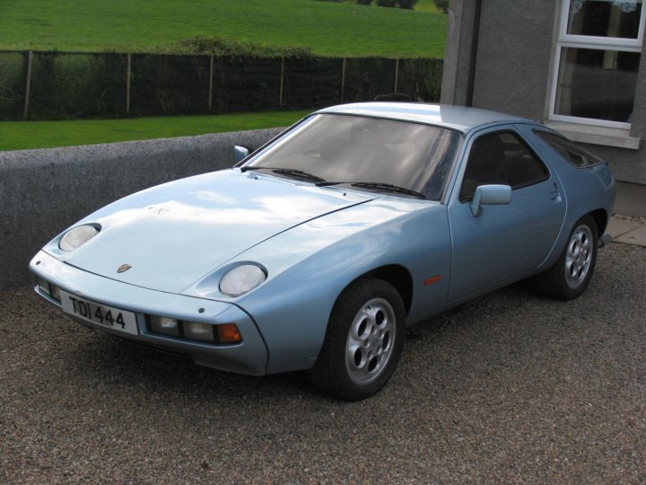 Pistonheads - The image captures a tranquil scene with a blue Porsche 944 parked on a gravel driveway. The car, boasting its iconic black and red interior, is positioned underneath a gray building. The contrast between the car's vibrant color and the gravel driveway forms an appealing visual. Two windows are open, hinting at a warm day, and the sky in the background suggests it might be a sunny afternoon.