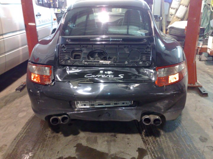 Hot Engine Wont Start Pistonheads - The image is a photograph featuring the rear view of an old, dark-colored car that appears to be in poor condition. The car's trunk lid is open, exposing its internal components. It sits on a lift, suggesting it is in a repair shop or garage setting. The lift's platform is visible underneath the car, featuring what seems to be a metal structure and a hoist system for raising or lowering vehicles. The car's taillights are visible, along with the left brake light. The vehicle has a license plate, but the text on the plate is not legible due to the image's angle and focus.