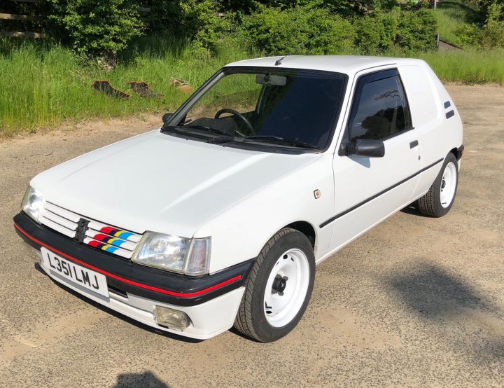 Peugeot 205 Dturbo Van - Page 1 - Readers' Cars - PistonHeads - The image displays a white and black sports car parked on what appears to be a paved surface, possibly a parking lot or driveway. The vehicle is modified with custom bodywork, including wide-body arches and a lower stance. It features an aftermarket aero package that includes side skirts, front and rear bumpers, and a large rear wing. The car has a distinctive color scheme with the hood and body accented in white, while the wheels are black with silver trim. There is no visible text or branding on the car that suggests it's for sale, but the style of the image, with its focus on the vehicle and the lack of contextual elements like a person or additional background features, suggests it may be intended for advertising purposes.