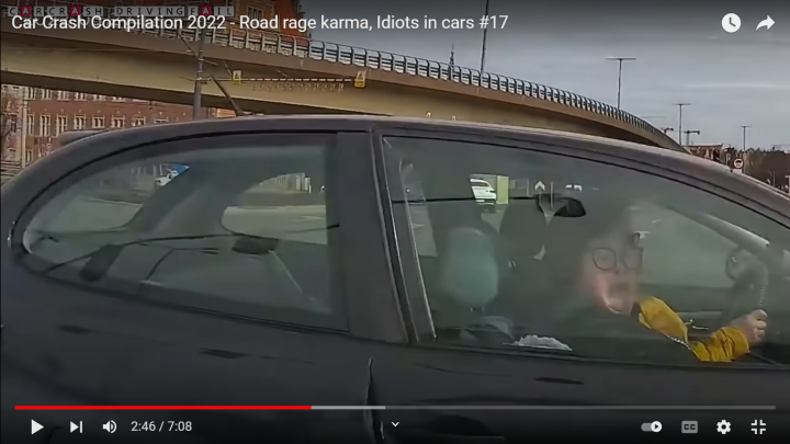 The "S**t Driving Caught On Cam" Thread (Vol 6) - Page 83 - General Gassing - PistonHeads UK - The image shows a car driving on the road. A person, likely the driver, is captured in the foreground of the vehicle's windshield. They appear to be using their phone while driving. In the background, there is an overpass and a bridge with railings. There is also text at the top that reads "CAR CRASH COMPILATION 2020" followed by a number "17". The style of the image seems to be a screenshot from a video platform, given the presence of the play button in the middle of the image.