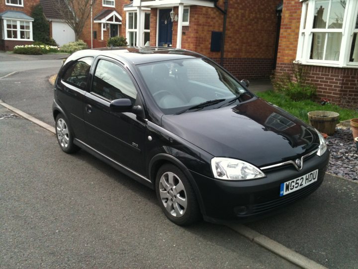 Pistonheads - In the image, a small black car is parked on the side of a street. The car is facing towards the right, and the license plate reads "WMS2HU." The setting appears to be a residential area, as evidenced by the adjacent house with a red brick exterior. The house has a clean, well-maintained appearance, with a neat front lawn and a clear view of the car's surroundings. In front of the house, there is a pathway leading to it, and to the side, there is a potted plant adding a touch of greenery to the scene. The car's position on the street, near the sidewalk and away from the flow of traffic, suggests that it is parked legally and safely. The overall image portrays a peaceful and orderly domestic setting.