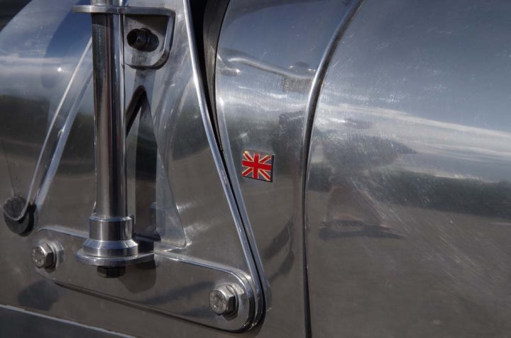 Door mirrors...? - Page 1 - Caterham - PistonHeads - The image showcases a close-up view of a car, likely made of stainless steel. The focus is on a door handle reflecting its surroundings. On the handle, there's a flag symbol, possibly representing British culture. This house-like emblem is an interesting detail on the metallic surface. The reflections and shadows subtly hint at a location with trees, creating an artistic contrast with the shine of the car.