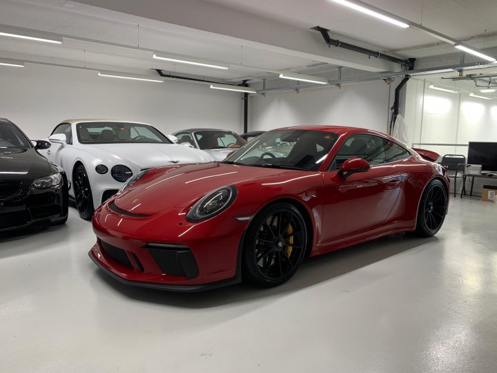 Are there really 47 GT3 tourings in the UK (C16) - Page 16 - 911/Carrera GT - PistonHeads UK - The image features a red sports car parked inside a spacious garage. The vehicle is characterized by its sleek design and luxurious finish, reflecting the high-quality craftsmanship of the manufacturer. It is surrounded by other luxury cars, suggesting an environment where such vehicles are stored or showcased. The lighting in the garage is bright, highlighting the car's vibrant color and shiny surfaces. There are no visible texts or distinctive brands in the image, keeping the focus solely on the automotive display.