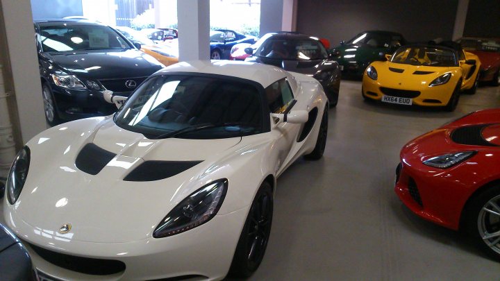 Hard Top & Black Wheels - Page 1 - Elise/Exige/Europa/340R - PistonHeads - The image captures a spacious indoor garage colored in a vivid shade of gray. The most eye-catching element is a collection of luxury cars, each with a distinct design - one is bright yellow; another is black; and the third is red. The cars are parked in a neat row, with the yellow one at the core and the black and red ones to its sides. This suggests a well-organized and stylish storage for these cars, highlighting their elegance and status-affirming presence.