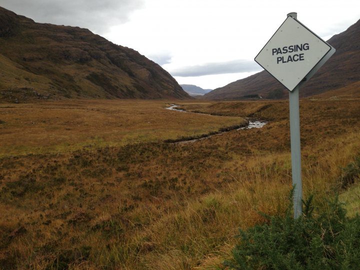 Random Photos : Part 4 - Page 137 - Photography & Video - PistonHeads - The image depicts a barren landscape where a sign has been placed for hikers or drivers. The sign, sitting in the grass and leaning a bit, reads 'PASSING PLACE'. The terrain around appears dry and desolate, which contrasts with the sign's message. The backdrop is a hilly or mountainous region with a creek visible in the distance, creating a natural path through the area.