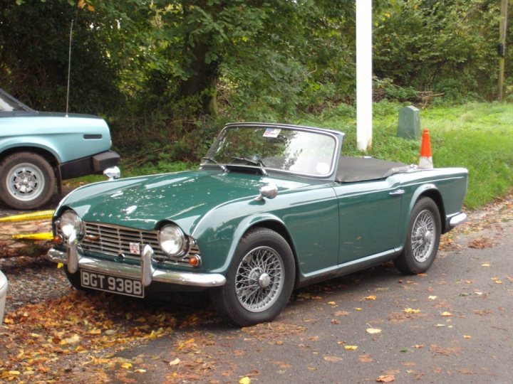 COOL CLASSIC CAR SPOTTERS POST!!! - Page 475 - Classic Cars and Yesterday's Heroes - PistonHeads - The image presents a charming scene on a grassy area. Dominating the view is a vibrant green MGB sports car, its metallic sheen reflecting an era of classic cars. The car is parked next to a white pole, indicating a designated parking spot. A concrete path, dotted with fallen leaves, meanders nearby, adding to the tranquility of the setting. Beyond the immediate foreground, the background reveals the presence of trees and bushes, hinting at a serene natural environment.