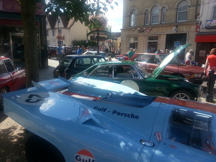 A car is parked on the side of the road - Pistonheads - The image captures a vibrant street scene where blue, green, and red Porsche cars are parked along a curb. Some cars are opened and parked on a slight incline. The cars are colorful and shiny, suggesting a well-maintained paint finish. Above them, the sky is clear, indicating a pleasant day, and there are trees right next to the sidewalk. People are scattered around the scene, which seems to be a public event or gathering related to classic cars.