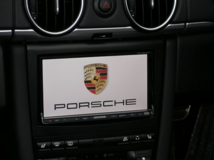 A laptop computer sitting on top of a desk - Pistonheads - The image shows the inside of a car's dashboard, focusing on the car's entertainment system display. A Porsche emblem is prominently displayed at the top of this screen, indicating it is a Porsche vehicle. The dashboard has various buttons and adjustments on its right-hand side, suggesting a level of customization for the driver's experience. The image is slightly blurred,