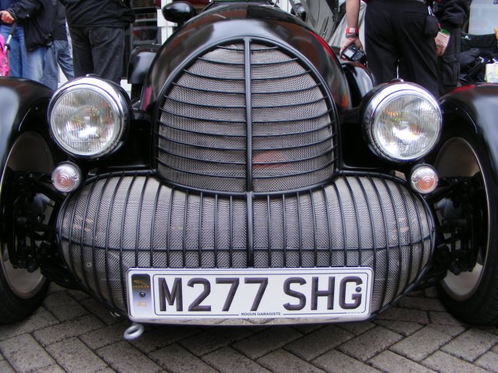 Ormskirk Motorfest, Sunday 26th August. - Page 1 - North West - PistonHeads - This image features a vintage car with a distinct grille and round headlamps, parked and positioned as to be viewed from the front left side. Moreover, it is adorned with a rectangular license plate that reads "M277 KBG" indicating its registration details. The wheels of the vehicle are detailed, and you can spot a small bit of the door handle on the passenger side. The car seems to be on display given the way it's parked, facing the viewer. Finally, there are a few indistinct objects and people barely visible in the background, suggesting an urban or public event setting.