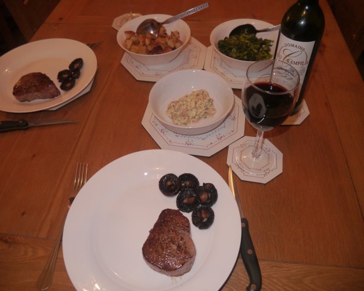 PH Cooking Competition #29 - STEAK  - Page 7 - Food, Drink & Restaurants - PistonHeads - The image presents a traditional dining setting. At the center of the image is a wooden dining table with a variety of dishes arranged neatly on it. The table setting includes a container of food, what appears to be a bowl of vegetables, and a plate of meat with essential utensils like a knife and a fork next to it. Further adding to the dining experience, there's a glass of red wine nearby, ready to complement the meal. The overall scene suggests a family or a small group enjoying a meal together.