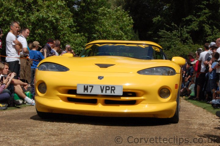 wilton house pics - Page 1 - Vipers - PistonHeads - In the center of the image stands a vibrant yellow sports car, the star of the show. It's parked on a dirt road, drawing the attention of a crowd of spectators. The crowd consists of people of different ages, with some sitting on the side of the road, their attention riveted on the sports car. The car features a number badge and a unique license plate, hinting at a possible competition or special event. A cheerful "Corvette" logo adorns the grille of the sports car, adding to its distinction. The image captures a moment of anticipation and appreciation for this impressive vehicle.