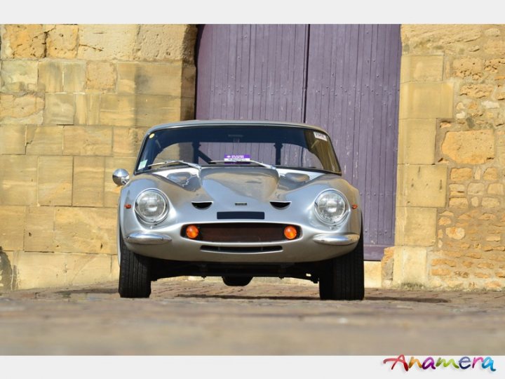 Early TVR Pictures - Page 36 - Classics - PistonHeads - The image features a vintage Alfa Romeo car, which is an open-top two-door vehicle. It is positioned in front of a beige-colored stone wall and is framed by a purple door on the right-hand side. The car's distinctive design and chromed finish, characterized by its round headlights, give it a timeless appeal. The pictorial watermark "Anamera" is present in the image, suggesting the photograph may be related to automotive art and photography in Budapest, Hungary.