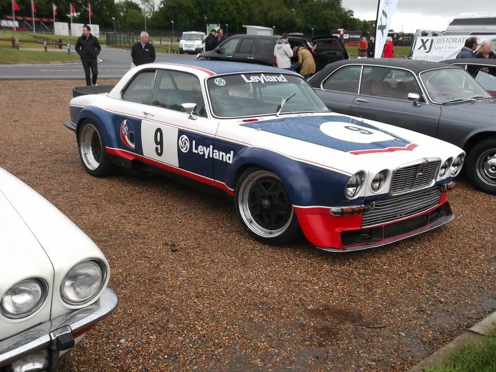 Rover P6, Jaguar XJ6... or something else? - Page 1 - Classic Cars and Yesterday's Heroes - PistonHeads - The image captures a classic scene of a road race, featuring a blue and white vintage race car as the main focus. The car is parked among other classic cars on a gravel surface, likely at a car show or exhibition. It's a spectacle of vintage automotive history with flames painted on the hood, the number "9" prominently displayed, and the word "Leyland" written across it. The atmosphere seems to buzz with the excitement of the race, and there are spectators walking around the parked cars.