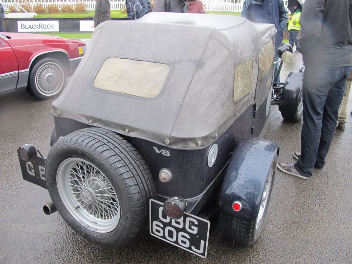 Tax Free Sunday 4th March 2012 - Page 3 - Goodwood Events - PistonHeads - The image shows a collection of vintage vehicles, including a small, gray docketing truck with a distinct silver paint finish. The truck is positioned with both of its rear wheels in front, adding to its unique appearance. The vehicle features a red or red-striped headlight, which matches the red spirit of the exhibit. The setting appears to be a paved area near grass, where people are standing around and looking at the vehicles, suggesting a vintage car show or exhibition.