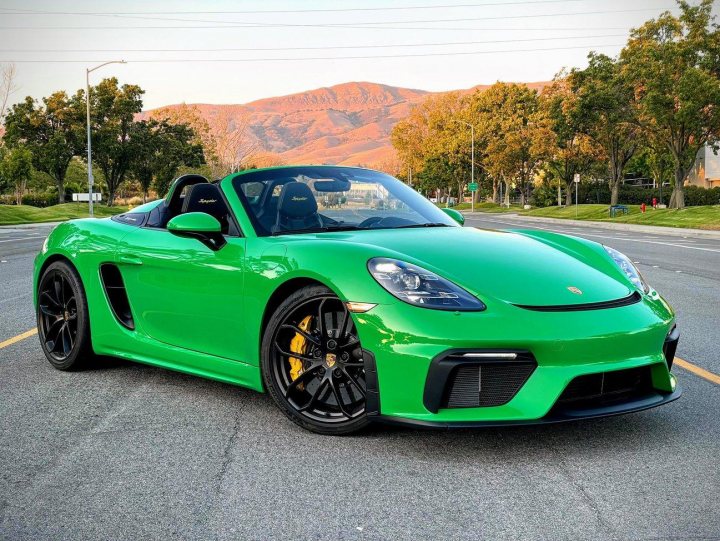 Pistonheads - This is a color photograph featuring a vibrant green sports car parked on what appears to be a city street. The car has a sleek design with a low stance, large wheels, and is adorned with a variety of badges and insignias that suggest high performance capabilities. It's positioned at an angle that gives a view of the front and side profile. In the background, there is a clear sky above and an urban setting below, including a building in the distance. The photo may have been taken during the golden hour given the soft lighting, which casts a warm glow over the scene.