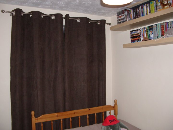 Pistonheads - The image shows an interior view of a room featuring a bed with a sturdy wooden headboard accompanied by wooden rails. The headboard is adorned with numerous books, filling the shelf attached to the wall above it. The room has a simple, clean decor, with the dominant color being a neutral shade, creating a serene atmosphere. The focal point is a large window dressed with three dark brown curtains that cover most of the window's surface. The curtains appear to be closed, creating a dimmer ambiance in the room. The floor is not visible in the image.