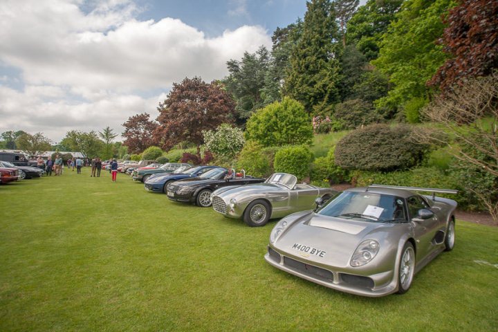 A black and white photo of a car parked in a field - Pistonheads - The image portrays a lively scene at a vintage car show situated in a lush green field. Numerous classic and sports cars are elegantly parked on the grass, showcasing an array of colors and models. People are seen mingling among the vehicles, socializing and appreciating the display. The sky overhead is filled with clouds, casting a natural backdrop to the event. The vibrant greenery contrasts beautifully with the shiny exteriors of the cars.