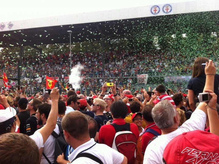 Monza GP - help an F1 know-nothing - Page 1 - Formula 1 - PistonHeads - The image captures a vibrant and lively scene at a football event. Thousands of fans are densely packed, filling the stands of the stadium. Many of them are holding up cameras, possibly recording the action on the field or taking selfies to capture their excitement. Tossing a ceremonial first item into the crowd, often a football, is being done as a symbolic gesture to commence the event. The atmosphere in the stands is ecstatic and energetic, indicative of the enthusiasm of the supporters.