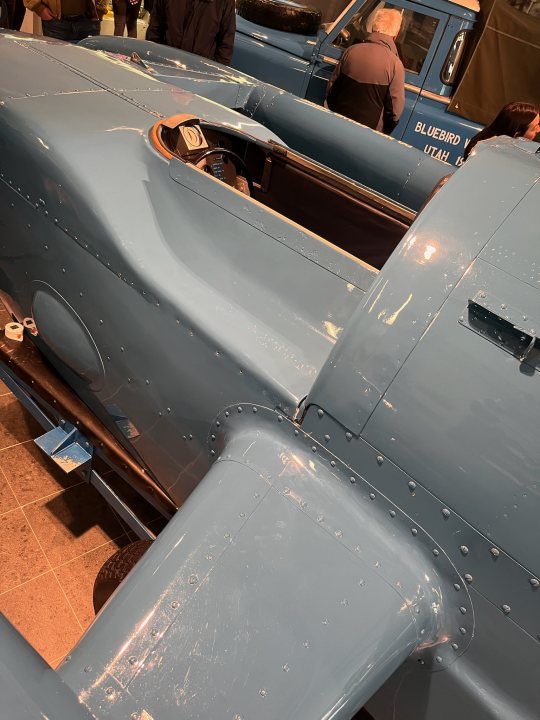 Pistonheads - The image showcases a vintage blue race car, which appears to be in excellent condition. The car is parked indoors, under soft lighting, suggesting it might be on display at a museum or exhibition. There are some people present in the background, possibly visitors or staff, adding a sense of scale to the vehicle. The car's design and color scheme give it a distinctly classic look, characteristic of early-to-mid 20th century racing machines.