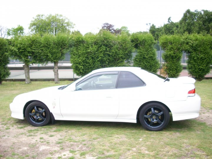 Resist Couldnt Pistonheads - The image captures a tranquil scene in a park or garden. A white two-door sports car is the focal point, parked on a grassy area. It features striking black rims, adding a touch of contrast to its overall white color. The backdrop of the image is a lush expanse of greenery, with a dirt path leading towards the car. In the distance, beyond the verdant foreground, a chain-link fence can be seen, suggesting the boundaries of the park or garden. The overall atmosphere is serene and quiet, a perfect setting to appreciate this beautiful white sports car.