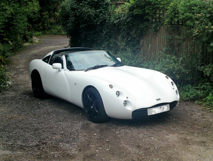 Pistonheads White Ibis Tuscan Tvr - The image shows a vibrant, small, white sports car on a dirt road. It has sleek lines and prominent bodylines, suggesting a racing origin. The vehicle is slightly angled, and the gravel surface around seems untrodden, providing a rustic background. The car's presence on such a path indicates that it is being used rather than being a pictorial prop. The image itself is a clear daytime shot with natural lighting, and it gives off a sense of motion and adventure.