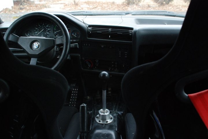 Post a picture of your track car! - Page 12 - Readers' Cars - PistonHeads - The image shows the interior of a vehicle, specifically focusing on the driver's side controls and accessories. From the perspective of the backseat, one can see into the cockpit. The steering wheel, located in the lower left area of the photo, appears to be standard in design, with the BMW logo in the center. To the left of the steering wheel is a handbrake control, located between the seats and above the gearshift. Directly behind the gearshift are two pedals, which are likely the accelerator and the brake pedal, although the exact configuration would need more context. The dashboard, which is shown in the middle section of the photo, features an array of controls and indicators, typical of modern vehicles. The hood of the vehicle also extends into the frame, partially visible above the dashboard. The overall ambiance suggests a quiet and still vehicle, possibly parked or not in use at the moment.