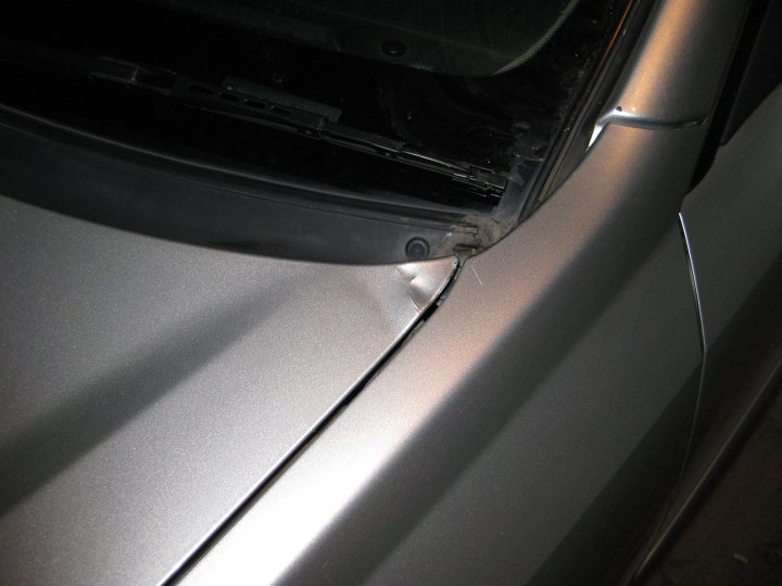 A close up of a luggage bag on a car - Pistonheads - The image shows a close-up view of a car's body, most likely focusing on aluminum-like material that appears to be metal. The car's surface has a shiny finish, which reflects light and creates a mirror-like effect on the surface below it. There is visible damage on the side of the car, specifically at the bottom edge of the car's body, which could be due to an accident or corrosion. The background is dark, drawing attention to the car's rim and the reflective surface beneath it.