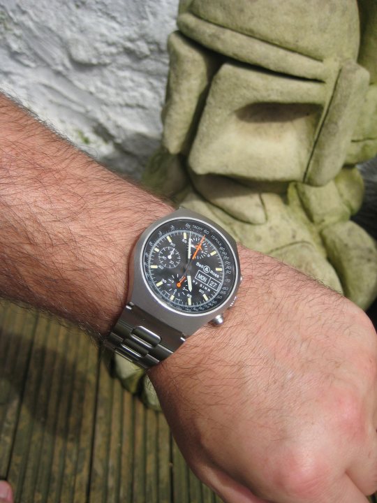 Watch Hard Wearing Pistonheads - This is a photograph close to a person's face, focusing on an analog wristwatch. The watch appears to be a diver's style with a black and white face. The watch's band is silver, and the case seems to be made of stainless steel. The person is holding their wrist, and the watch is positioned at an angle in the frame. The background is blurred, emphasizing the elegance of the watch itself. The lighting suggests it might be daytime with natural light being diffused.