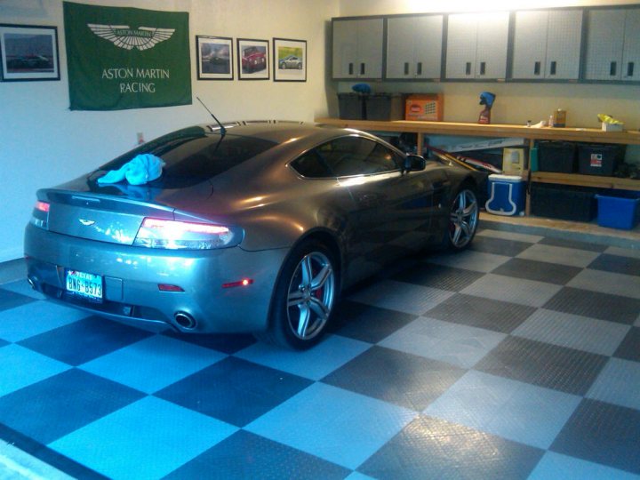 Glass Tinted Vantage Pistonheads - The image shows a silver Aston Martin sports car parked indoors on a black and white checkered floor. The vehicle is positioned at a slight angle to the viewer and appears clean and well-maintained. Along the rear wall of the room, there are framed pictures of racecars and a banner with the text "Martin Racing and Aston Martin." The atmosphere suggests a dedicated racing enthusiast's space.