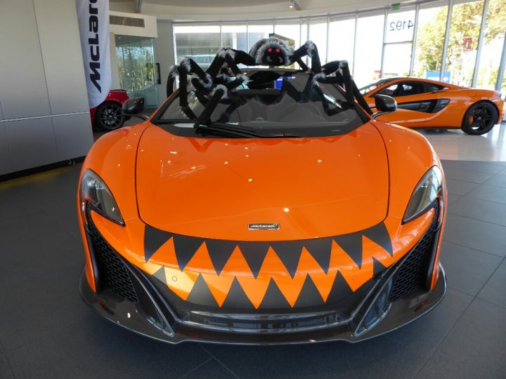 RE: McLaren 570S: Review - Page 3 - General Gassing - PistonHeads - The image features a vibrant orange sports car that captures attention with its Halloween-themed car wrapping. This customization has transformed the car, adding a playful and festive touch to its sleek body. The car is displayed in a showroom, with a black spider on the ceiling and another spider on the car's roof, contributing to the eerie ambiance of the scene. The showroom itself is modern and spacious, with large windows allowing natural light to flood in.