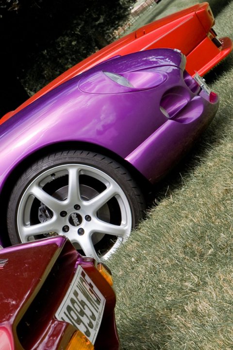 Manor Motors Pistonheads - The image captures a scene of two classic cars parked side by side on a grassy surface. Dominating the front of the image is a vibrant purple sports car, its sleek lines and reflective paint shining subtly in the light. Next to it, in the background, is a red convertible, its top neatly folded down. Both cars are facing towards the right side of the image, as if poised to take off into the clear sky above. The ground they rest on is a lush green, providing a stark contrast to the rich hues of the cars. Despite being inanimate form, the image conveys a sense of anticipation, as if these cars are ready to roar into motion at any moment.