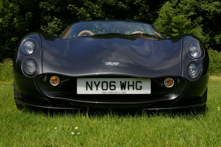 Your Best Tuscan Pic... - Page 6 - Tuscan - PistonHeads - The image showcases a black convertible sports car with a sleek design, parked in a grassy area. It displays a license plate of NY06 WHG, indicating its location or registraion. The car's bodywork has shades of blue, suggesting it might be in a shadowy environment or at the end of a long day, as the paintwork looks slightly worn or faded. The car exudes a sense of speed and exclusivity, typical of such high-end automobiles. The setting appears serene and private, with the car as the main focus, highlighting the contrast between the elegance of the vehicle and the natural surroundings.