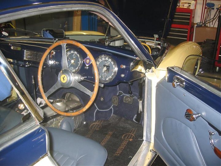 A close up of a train on a train track - Pistonheads - The image shows the interior of an old-style car from the perspective of the cockpit, focusing on the open driving area. There is a steering wheel in the foreground, characterized by its classic design with a marque emblem. Behind the wheel, the hood of the car is propped open, revealing a mix of mechanical and electrical components. The seats, interior door panels, and dashboard are visible. The colors of the exposed interior are a mix of blue, metal fixtures, and parts painted in a shade of yellow. In the background, various garage tools can be seen, suggesting that this car may be under maintenance or standing in a maintenance area.