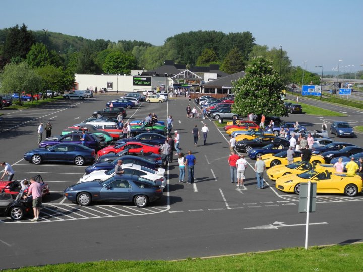 Gordano this morning en route to cwc - Page 1 - South West - PistonHeads - The image showcases a bustling auto show, where an abundance of brand new luxury and sports cars are parked. Spectators can be seen strolling around the show, admiring the sleek designs and shiny exteriors of the vehicles. The display is set on a grassy area, surrounded by a parking lot filled with spectators' cars. In the background, a dealership appears to be hosting the show.