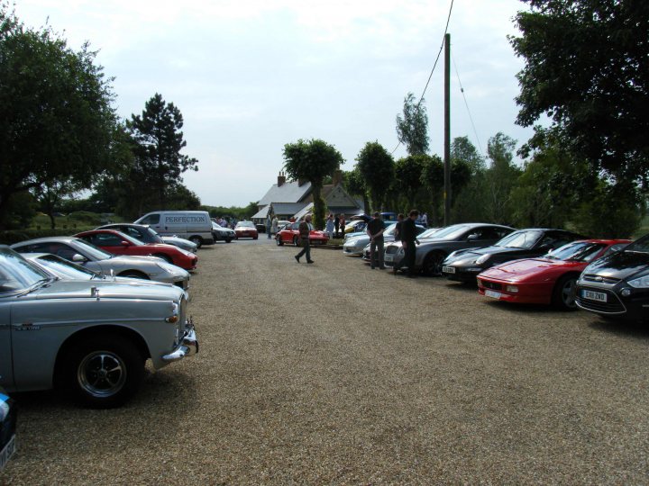 Breakfast Meeting, The Hare, Roxwell 4th June - Page 1 - Kent & Essex - PistonHeads - This image presents a captivating scene of a car yard, where a row of cars and a truck is neatly parked. A group of people can be seen engaging in conversation next to the cars. The variety of cars includes a mix of traditional models and innovative designs, suggesting a diverse vehicle selection. In the middle of the yard, a charming house with a matching garage and a brick driveway adds a touch of homeliness to the scene. The ground is smoothly paved, reflecting the daylight and providing an excellent surface for parking. Overall, the image conveys a sense of leisure and excitement about automobiles.