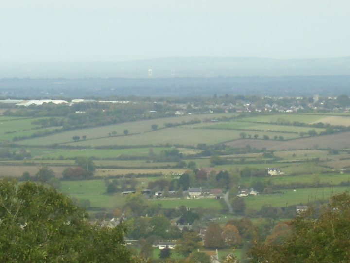 Region Owners Western Pistonheads October - The image presents a picturesque view of a rural landscape, where the countryside is dotted with houses. The pattern of the fields suggests an agricultural setting, with patches of green interspersed with areas of brown, indicative of croplands. The rolling hills and the blurred horizon give a sense of depth and distance, while the presence of trees adds a touch of greenery to the overall rural scene. The overcast sky indicates a cloudy day.