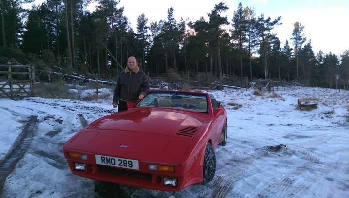 Winter Wedges - Page 2 - Wedges - PistonHeads - This image captures a man standing next to an old red roadster parked in a snowy field surrounded by trees. The man is wearing a dark jacket and appears to be at ease in the wintery environment. The car appears to be a classic model, with a distinctive round headlight design. The ground is covered with a layer of snow, indicating that the photo was taken during the winter season.