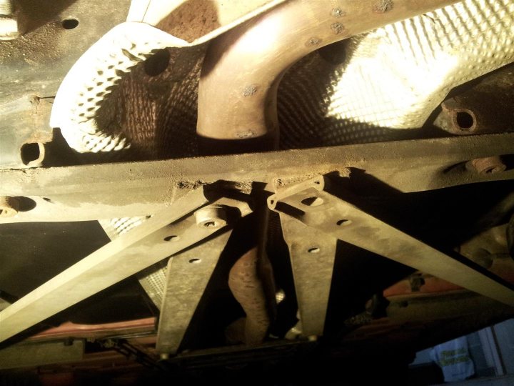 A pair of scissors sitting on top of a wooden table - Pistonheads - The image provides a close-up view of the undercarriage of a vehicle, focusing on mechanical components. The primary subject appears to be a hydraulic cylinder, which is situated near another cylindrical component. These cylinders are mounted on some sort of support bracket, which is connected to what seems like a crossmember in the vehicle's chassis. The overall scene suggests a setting where vehicle parts are being installed, serviced, or inspected.