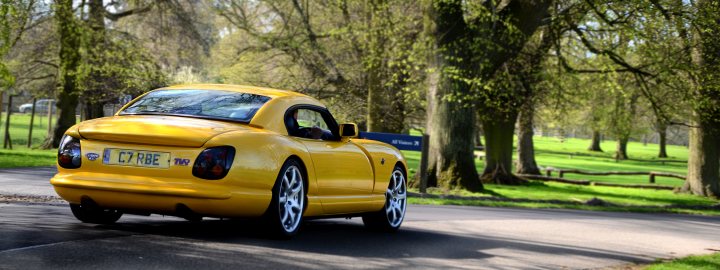 Burghley House 2014 - Pictures! - Page 2 - TVR Events & Meetings - PistonHeads - This image features a yellow car on a road with trees in the background. The car appears full-sized and has a classic design. The car is facing forward, with the front wheel slightly turned to the side. The license plate is visible and shows the letters "C7 RA6." The trees are in the foreground, suggesting that the car is driving along the side of a road.