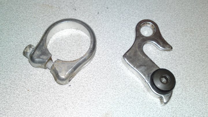 Dual Suspension Recumbent??? - Page 2 - Pedal Powered - PistonHeads - The image shows two metal components with a shiny silver finish, positioned against a white background. On the left, there is a rounded ring, which appears to be the top part of a boot clamp, commonly used with hiking boots. On the right, there is an L-shaped bracket, which looks like a part of a mechanical or automotive gadget. Both objects seem to be made of steel or a similar alloy, and are identical in their construction, indicating they may be a pair.