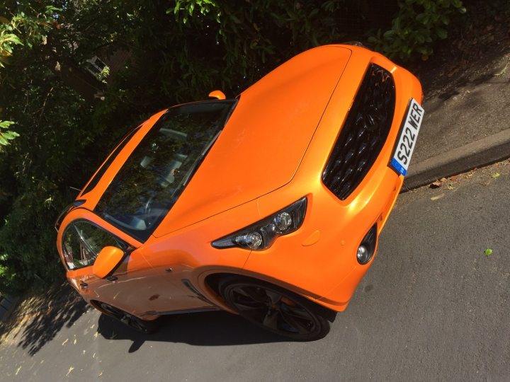 Cheap cars that get lots of attention...? - Page 5 - General Gassing - PistonHeads - The image shows a vibrant orange sports car parked on the side of a road. The car has a sleek design with a prominent front grille and angular headlights. There's visible branding, including a badge on the front grille. The vehicle appears to be in good condition, suggesting it might be new or well-maintained. The car is positioned next to a paved area with vegetation, indicating an outdoor setting. There are no people present in the image.